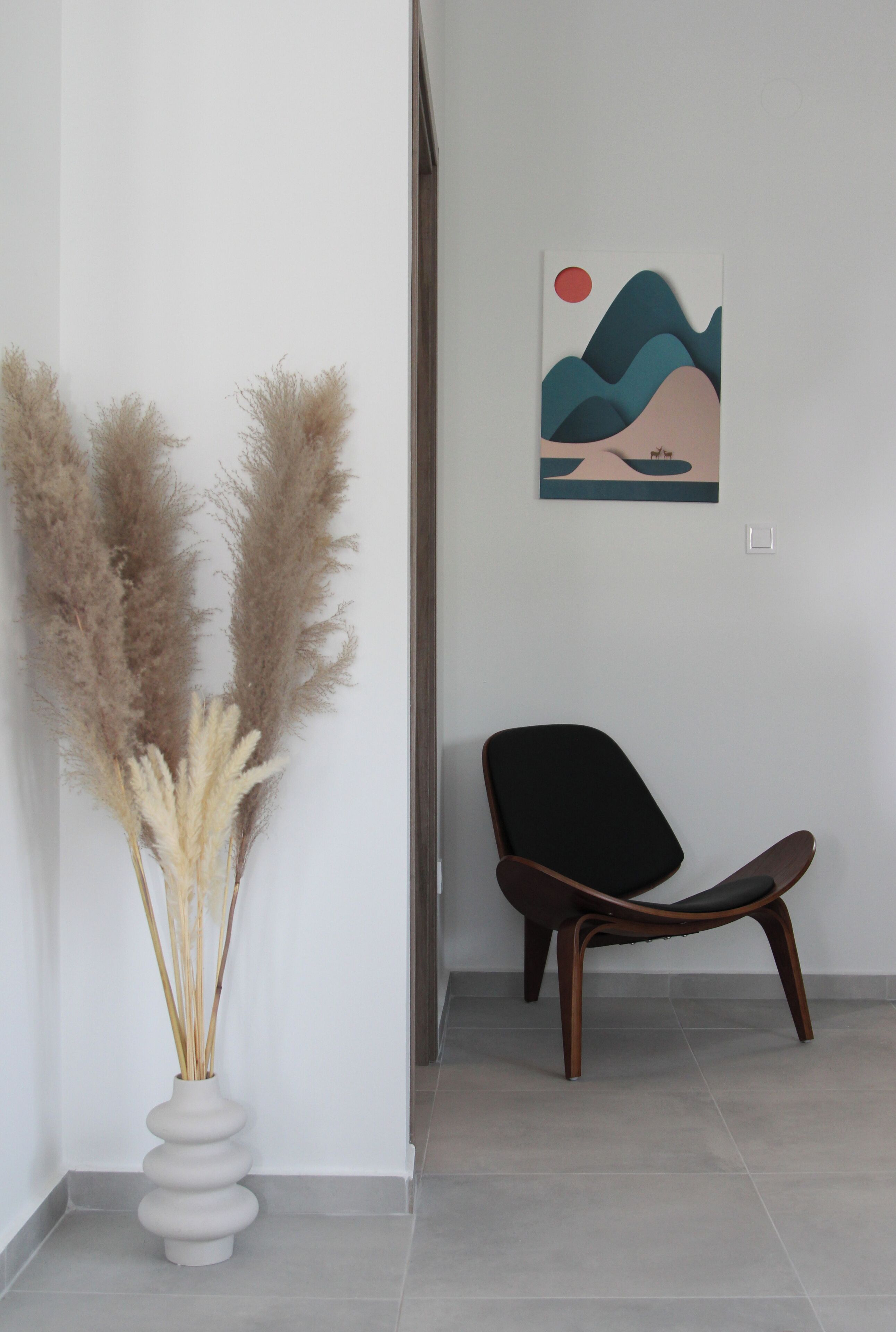A modern interior with a white vase of pampas grass, a black chair, and a wall-mounted abstract painting.