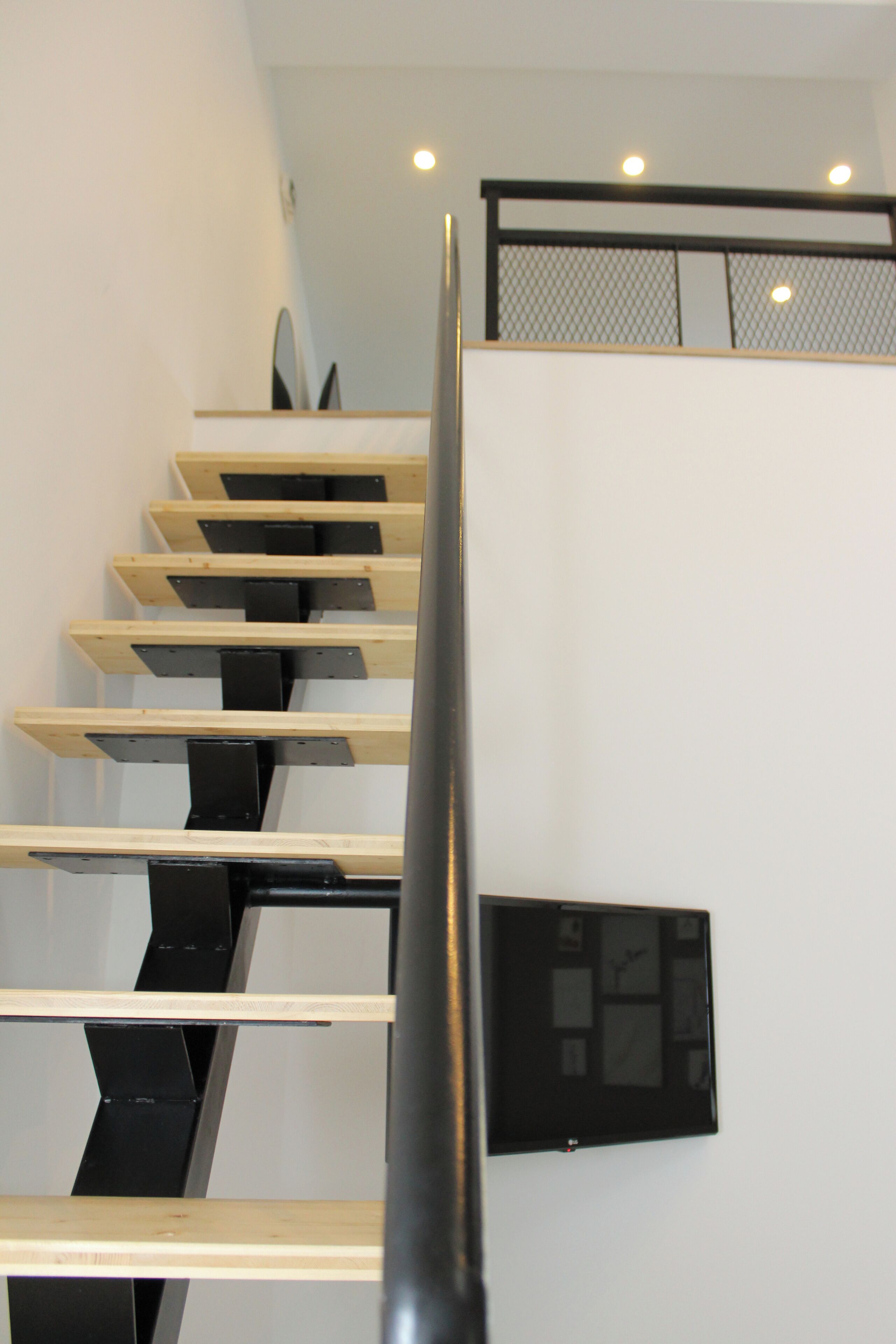 A modern staircase with wooden steps and black railings, leading to a landing with a black-framed picture.