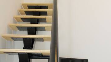 A modern staircase with wooden steps and black railings, leading to a landing with a black-framed picture.