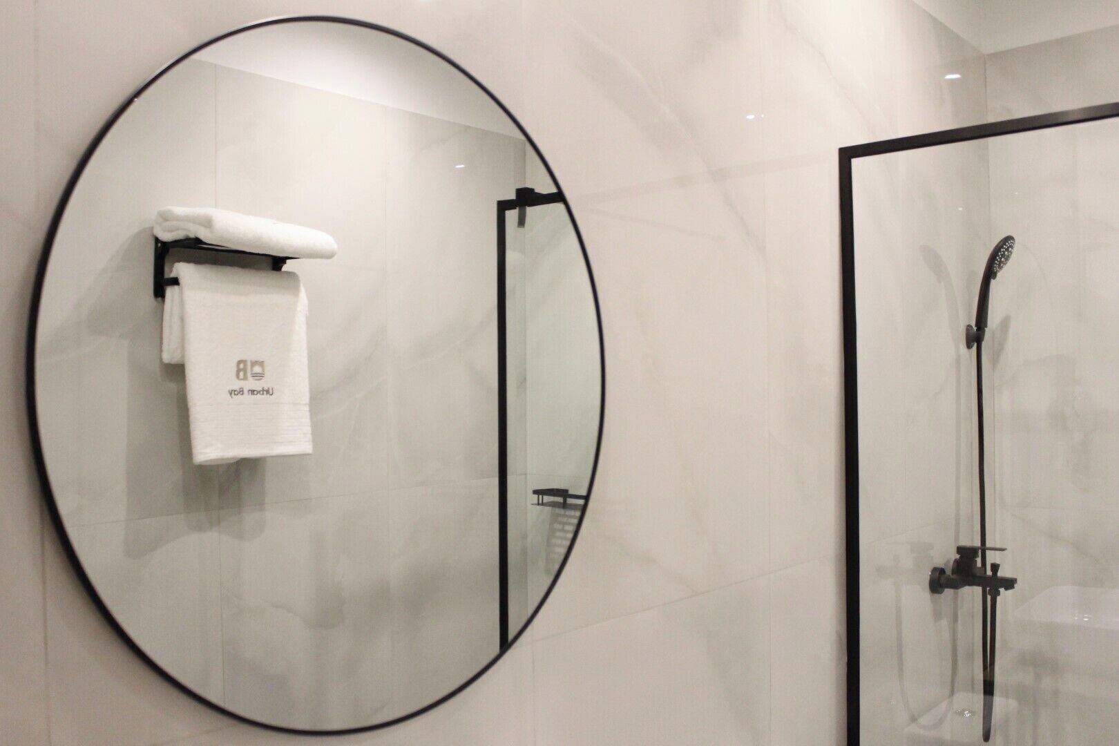 A modern bathroom with a large mirror, a towel rack with a towel, and a glass shower enclosure.
