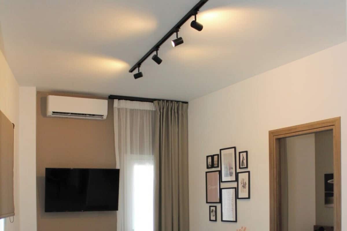 A modern living room with a sofa, a coffee table, a TV mounted on the wall, and a bed with a wooden headboard.