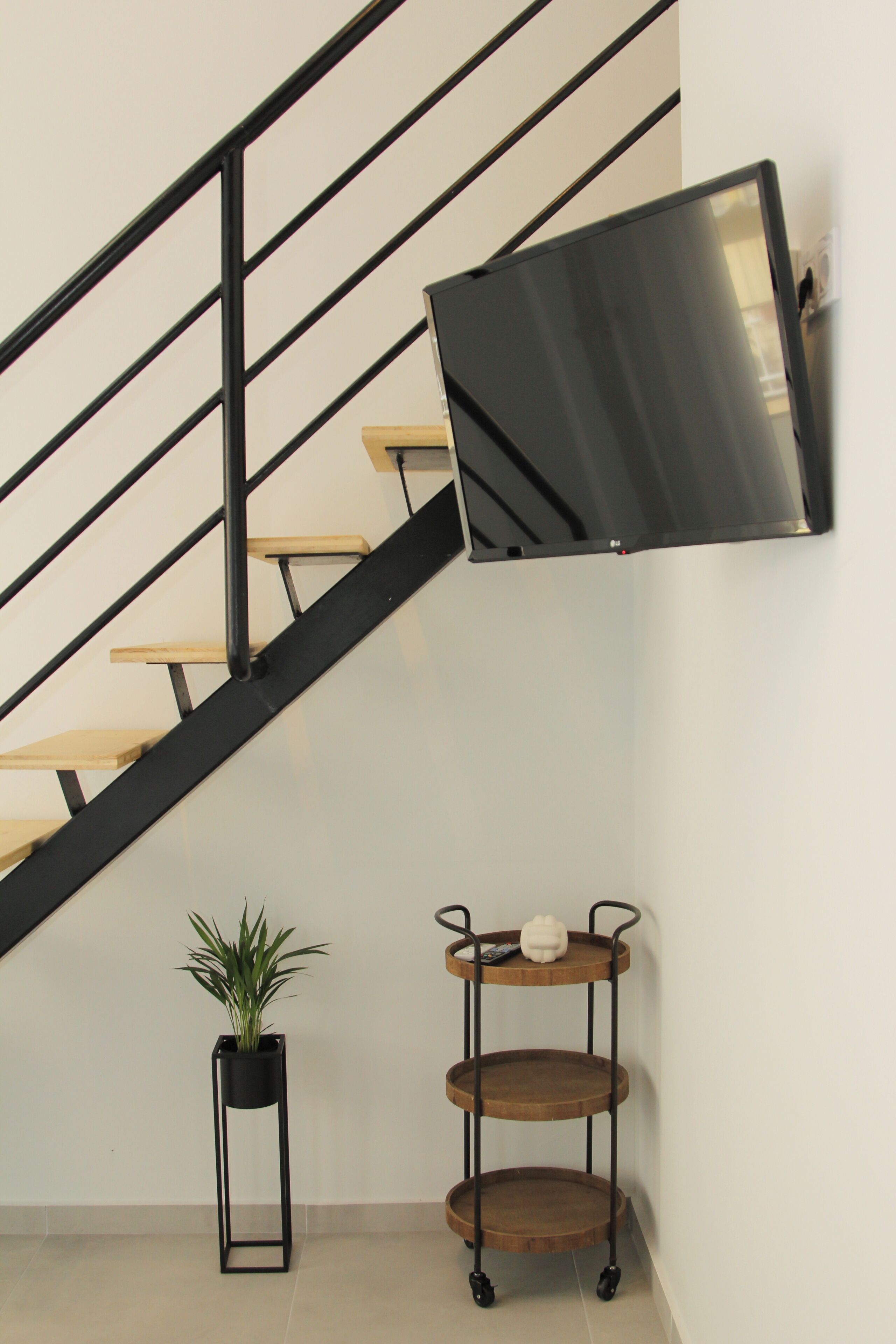 A staircase with a black metal railing, a wooden floor, a potted plant, and a wooden shelf unit with a white spherical object on top.