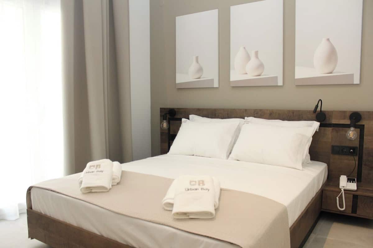 A hotel room with a neatly made bed, two bedside tables, a wall-mounted phone, and three framed vases on the wall.