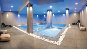 Piscina interior moderna con suelo azul, rodeada de pilares de piedra y bancos.