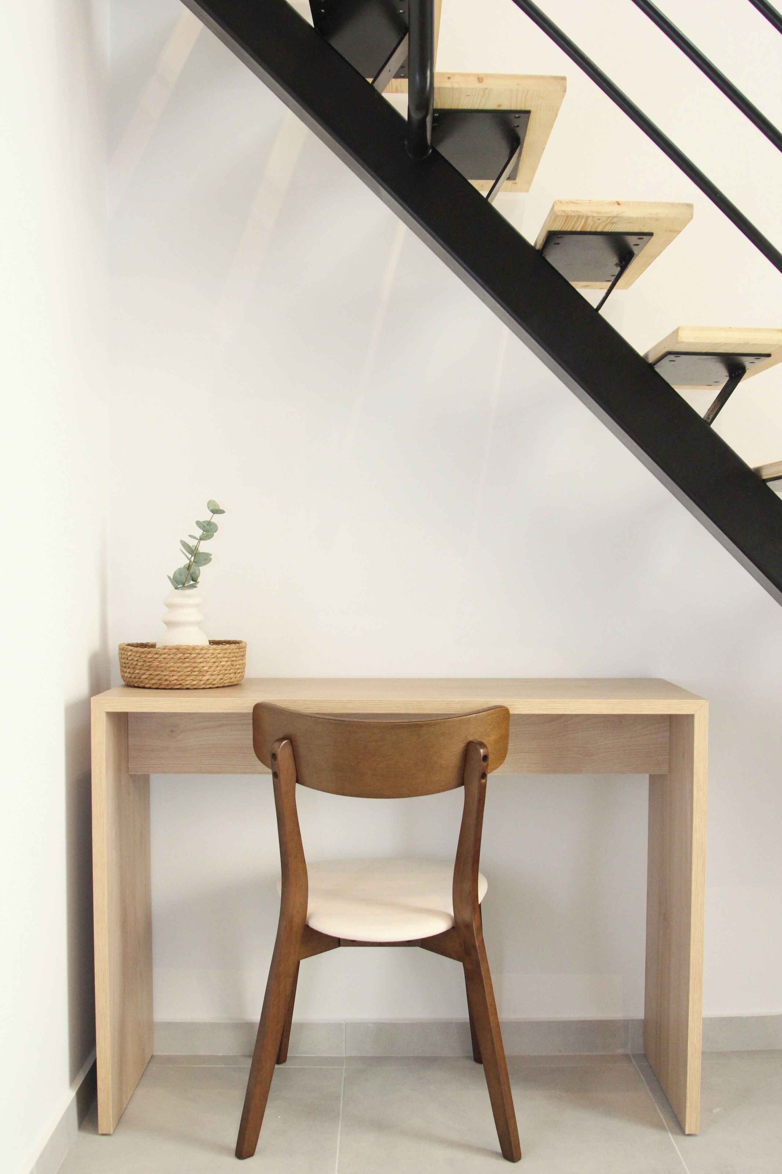 A wooden desk with a chair, a woven basket, and a small potted plant.