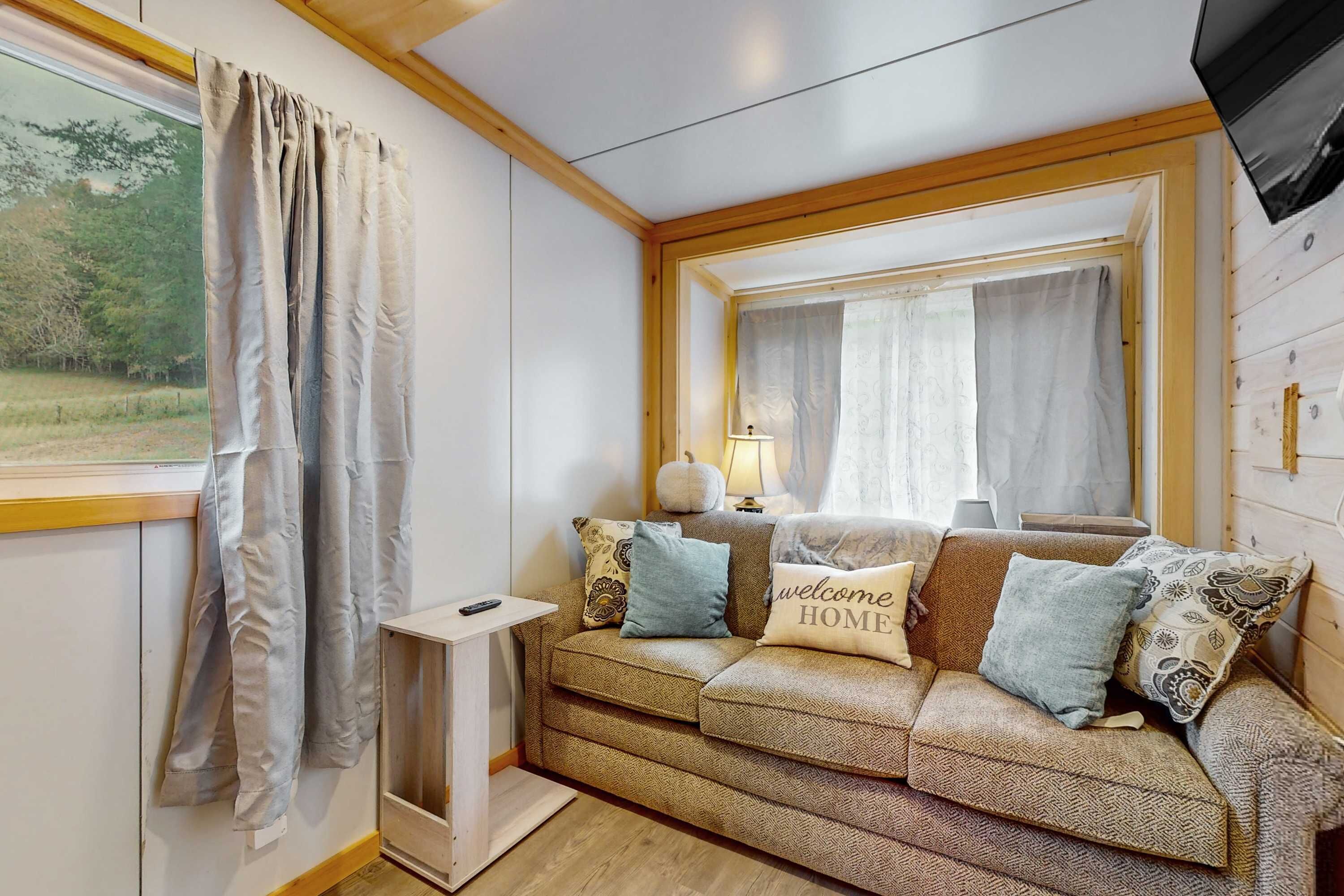 Una sala de estar acogedora con sofá, almohadones, una lámpara y un televisor.