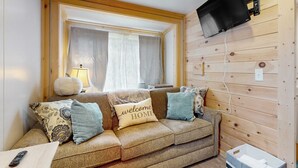 Ein gemütliches Wohnzimmer mit einer Couch, einem an der Wand befestigten Fernseher und einem Fenster mit Vorhängen.