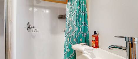 A bathroom with a shower, a sink with a chrome faucet, a bottle of soap, and a patterned shower curtain.