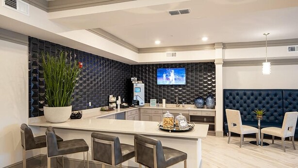 Una cucina moderna con isola centrale, sgabelli da bar, una zona salotto con una panca imbottita scura e un televisore a parete.