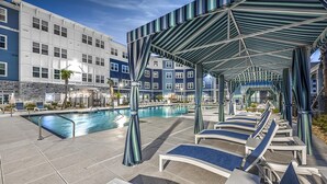 Area piscina con lettini da relax e una zona salotto coperta, circondata da un edificio a più piani con facciata in pietra.