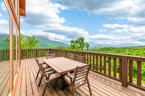 Una terraza de madera con mesa y sillas, con vistas a un paisaje verde y montañas.