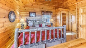 A wooden cabin bedroom with a bed, two bedside lamps, a ceiling fan, and a window with curtains. - Homey Cabin, Sleeps 8, Hot Tub, Theater, Games, Views (Pigeon Forge)