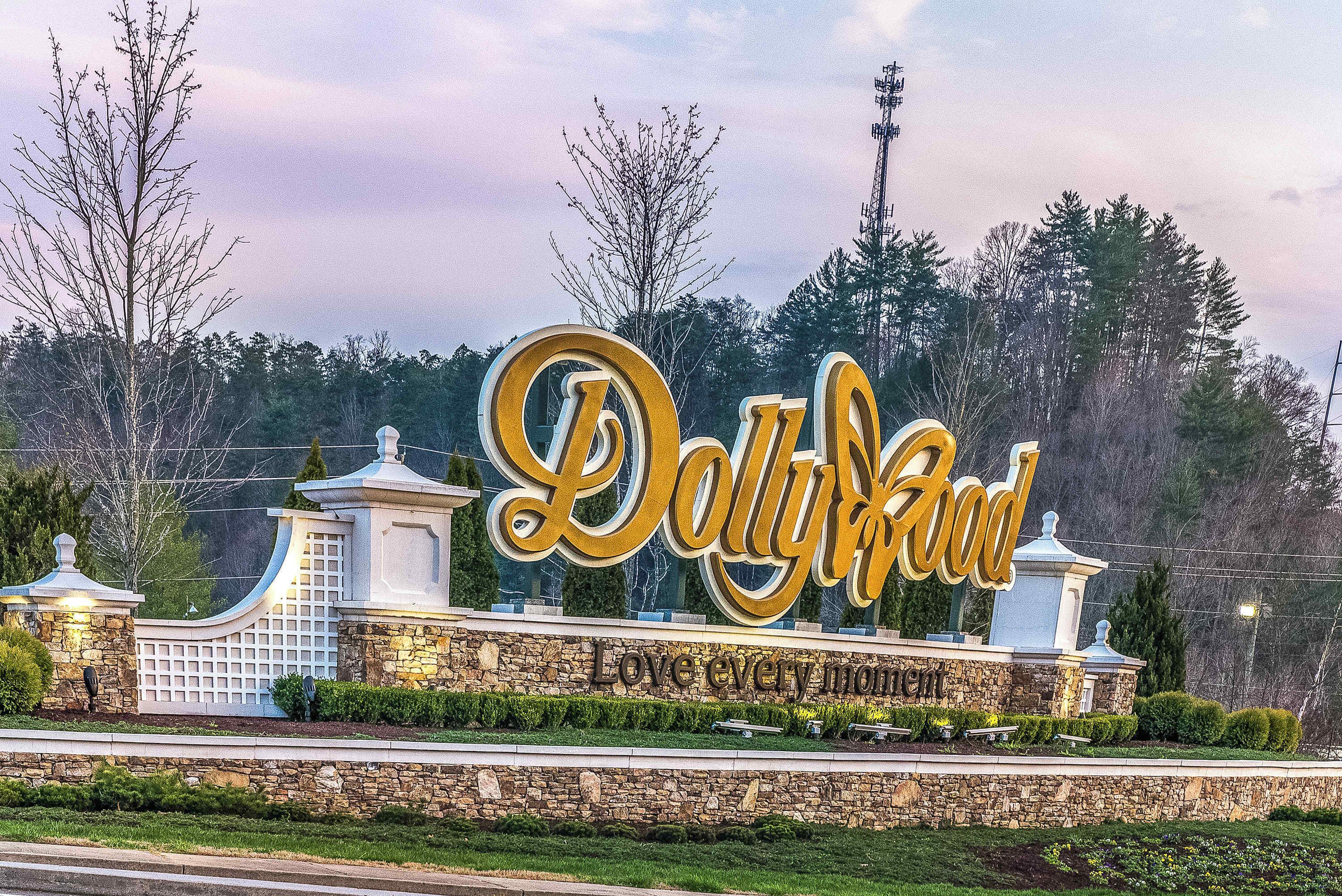 A sign for Dolly Parton-themed park with a stone wall and decorative elements.