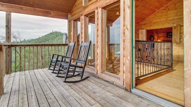 A wooden deck with rocking chairs and a glass door leading to an interior space. - Homey Cabin, Sleeps 8, Hot Tub, Theater, Games, Views (Pigeon Forge)