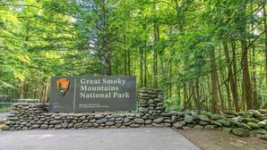 A sign for Great Smoky Mountains National Park with a stone wall and forested background. - Homey Cabin, Sleeps 8, Hot Tub, Theater, Games, Views (Pigeon Forge)