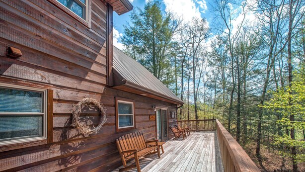 Une cabane en bois dotée d’une terrasse, de bancs et d’une rambarde, offrant une vue sur une forêt.
