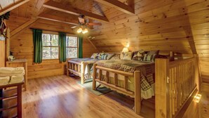 Une cabane chaleureuse avec une chambre à coucher en mezzanine, un plancher en bois, un ventilateur de plafond et une fenêtre avec des rideaux.