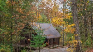 Un chalet rustique entouré du feuillage automnal, doté d’une terrasse en bois et d’un porche abrité.