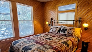 Een slaapkamer met houten lambrisering, een groot bed, twee bedlampen en een raam met jaloezieën.
