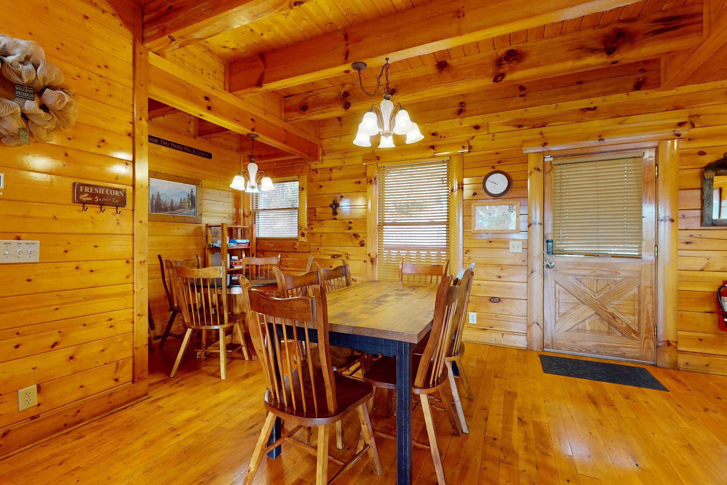 Un intérieur en bois comprenant une table et des chaises, des murs en bois, une horloge et une porte ornée d’une croix.