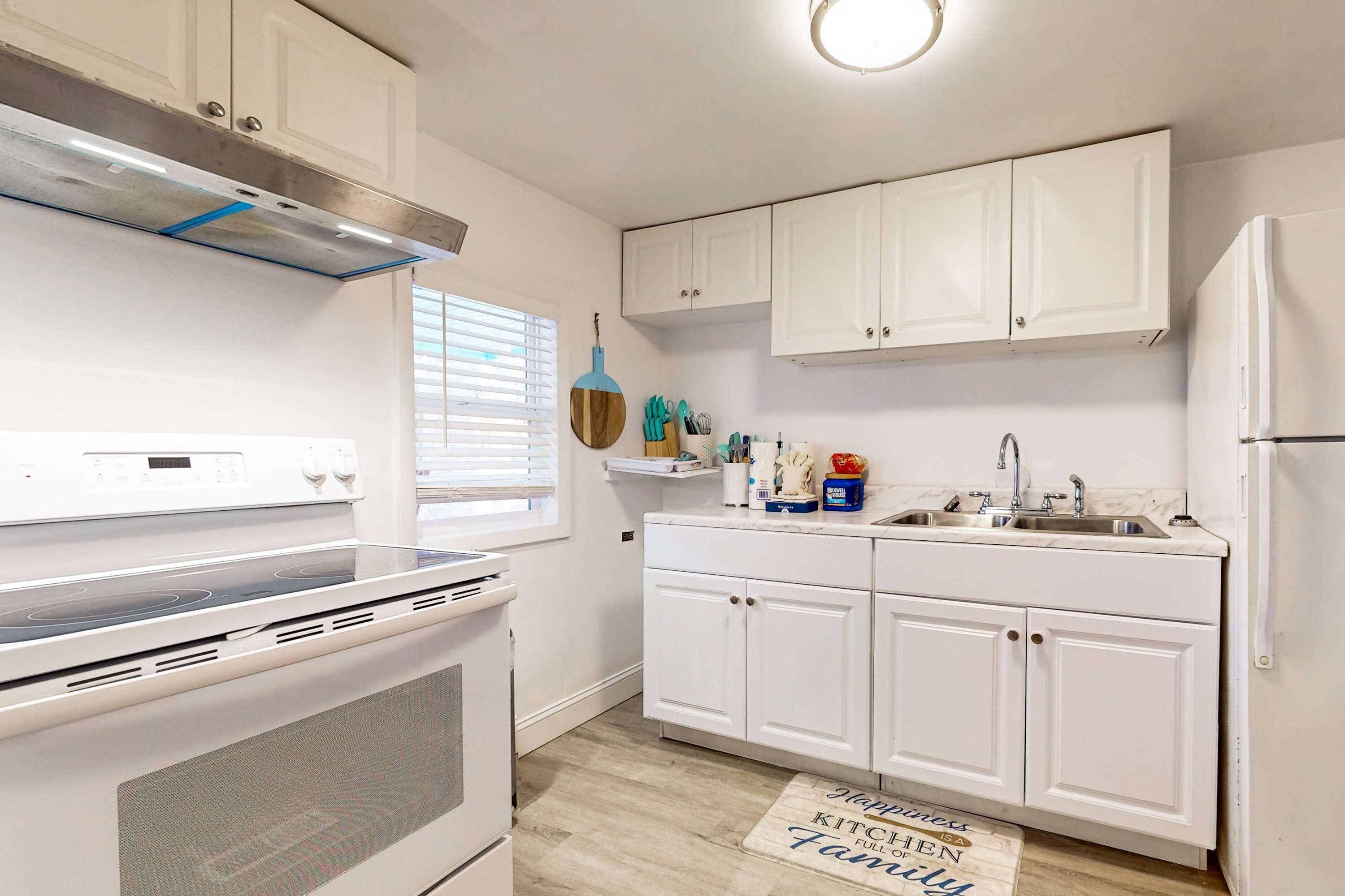 A modern kitchen with white cabinets, a stainless steel range hood, a built-in oven, a sink, and a refrigerator.