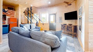 L’intérieur chaleureux d’un chalet avec un canapé, un téléviseur et un escalier menant à un étage supérieur.