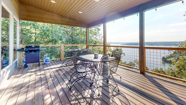 Une terrasse en bois avec un barbecue, des tables et des chaises, donnant sur un lac.