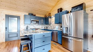 Une cuisine moderne avec un plafond en bois, des armoires bleues, des appareils électroménagers en acier inoxydable et un plancher en bois.