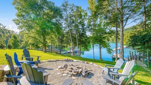 A lakeside outdoor seating area with Adirondack chairs, a fire pit, and a view of the lake and docked boats. - Spacious Norris Lakefront Retreat・Firepit・Hot Tub (Maynardville)