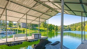 A covered dock area with a bench, a Yamaha boat, and a view of a lake with boats and greenery in the background. - Spacious Norris Lakefront Retreat・Firepit・Hot Tub (Maynardville)