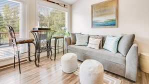 A cozy living room with a grey sofa, two ottomans, a metal table with chairs, and a painting on the wall. - Spacious Norris Lakefront Retreat・Firepit・Hot Tub (Maynardville)