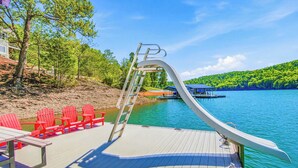 A deck with a ladder, red chairs, and a boat on a calm lake. - Lakefront Retreat N Norris Lake・Dock W Slide・Games (LaFollette)