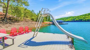 A deck with a ladder, red chairs, and a boat on a calm lake.