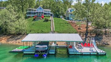 A lakeside property with a dock, a covered boat launch, and a large house with a porch.