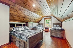 Une chambre avec un plafond en pente, un plancher en bois et deux lits dotés de têtes de lit assorties.