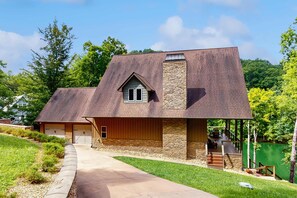 Une maison moderne avec une cheminée en pierre, une véranda et une allée menant à un garage.