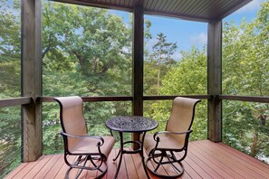 Une terrasse en bois avec deux chaises et une table, donnant sur une zone boisée.