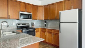 Una cocina con armarios de madera, un refrigerador de acero inoxidable, un microondas, una estufa y encimeras de granito.