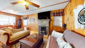 Un salon chaleureux avec une cheminée en pierre, des murs en bois et un ventilateur de plafond.