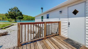 En træterrasse der fører hen til en hvid campingvogn med skorsten, et lille vindue og en dør med et spionglas.
