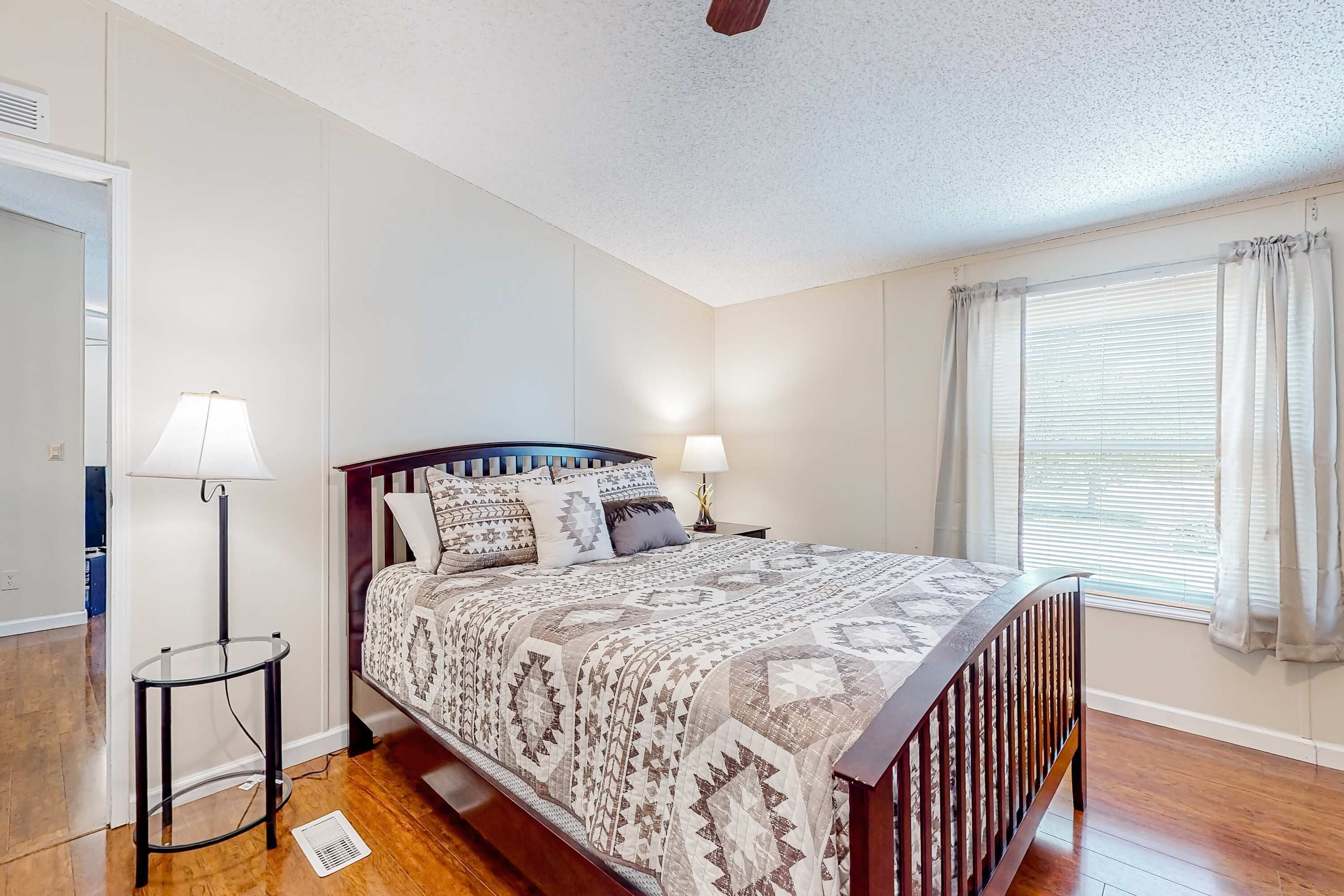 A bedroom with a bed, bedside lamps, a window with curtains, and a small table.