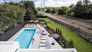 Une piscine sur le toit, dotée de chaises longues et de parasols, entourée d’une pelouse et avec une voie ferrée en arrière-plan.
