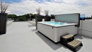 Une terrasse sur le toit équipée d’un jacuzzi, de chaises longues et de jardinières.