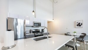 Une cuisine moderne dotée d’appareils électroménagers en acier inoxydable, d’un îlot central blanc et d’un coin repas avec une table et des chaises.