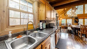 A wooden cabin with a kitchen featuring two sinks, a dining area with a table and chairs, and large windows providing natural light. - Upscale Cabin W Hot Tub, Sleeps 22・Game Room・Pool (Sevierville)