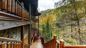 A wooden staircase leading to a balcony with a stone wall, surrounded by autumn foliage. - Upscale Cabin W Hot Tub, Sleeps 22・Game Room・Pool (Sevierville)