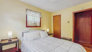 Un dormitorio con una cama, mesitas de noche, un armario auxiliar, una puerta de madera y una ventana con cortinas.