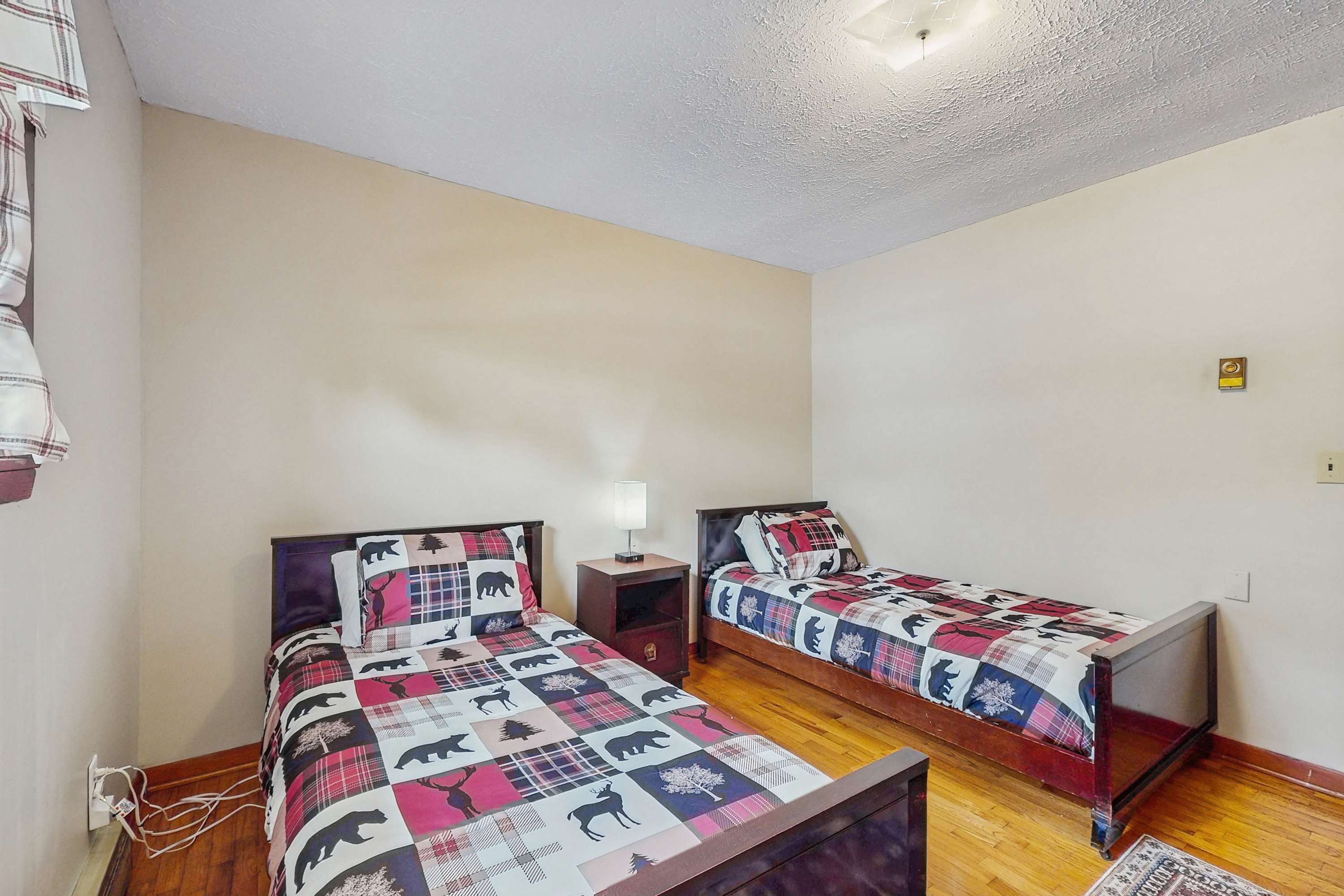 A room with two beds, each with a patterned bedspread and headboard. There is a nightstand with a lamp between the beds.