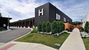 A modern hotel with a prominent 'H' logo, a covered outdoor area, and well-maintained landscaping. - Landing | Beautiful 1BD, Pool, Gym (Royal Oak)