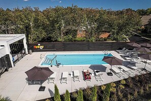 A rooftop pool with lounge chairs and umbrellas, surrounded by trees and a building in the background. - Landing | Stunning 1BD, Gym, Pool (Royal Oak)